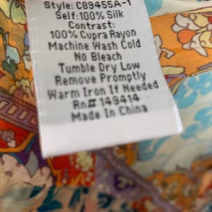 May include: A white clothing tag with black text, including the style number C89455A-1, fabric composition, and care instructions. The tag is set against a colorful patterned fabric background.