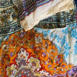 May include: A collection of colorful fabric pieces with intricate floral and geometric patterns. The fabrics feature a mix of orange, blue, purple, and cream colors, creating a vibrant and artistic display. The textiles appear to be lightweight.