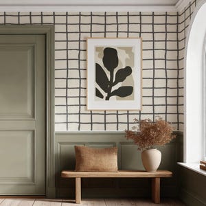 May include: Interior scene with a sage green door, a framed botanical print, and a wooden bench with a pillow. The walls are adorned with a grid pattern. A vase with dried flowers sits on the bench, and a window is visible.