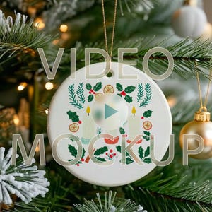 May include: A white ceramic Christmas ornament with a festive design of candles, holly, and orange slices. The ornament hangs from a gold string against a blurred Christmas tree background. Text overlay reads "VIDEO MOCKUP".