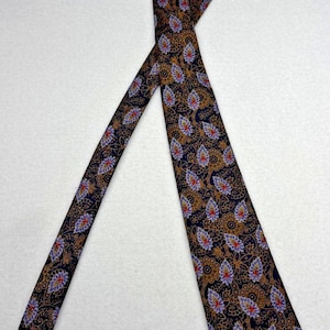 May include: A necktie featuring a dark navy blue background with an intricate repeating pattern of golden-brown filigree swirls and stylized teardrop-shaped motifs in shades of light blue, purple, and small accents of bright red throughout.