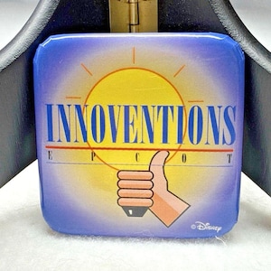 Puede incluir: Un botón cuadrado con un fondo degradado en azul y morado y un gráfico de sol amarillo. El texto dice INNOVENTIONS y EPCOT en azul, acompañado de un icono de mano estilizada con el pulgar hacia arriba. El logotipo de Disney es visible.