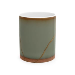 May include: A cylindrical mug with a sage green exterior and a white interior. The mug features gold-coloured lines, and a brown base and rim. The mug is a unique piece of drinkware.