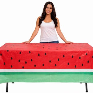May include: A rectangular tablecloth featuring a watermelon design. The top is red with black seed details, transitioning to a white stripe and a green base. The tablecloth is on a table with black legs.