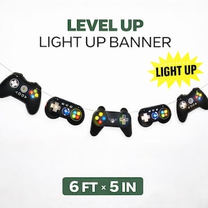 May include: A black light-up banner with controller shapes, featuring the text "LEVEL UP LIGHT UP BANNER". The banner is 6 ft long and 5 inches wide. The controllers have colorful buttons and a starburst with the words "LIGHT UP".