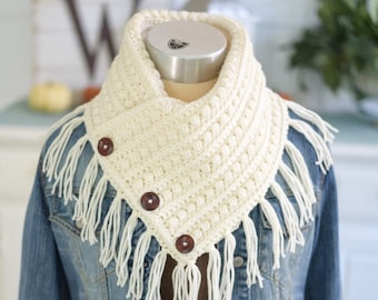Puede incluir: Bufanda de cuello de ganchillo color crema con flecos y dos botones marrones. La bufanda se lleva sobre una chaqueta vaquera. El cuello tiene un patrón de puntadas texturizado y está diseñado para llevarse alrededor del cuello.