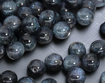 May include: A collection of dark blue, round beads with a speckled, glittery appearance. The beads are smooth and shiny, with a reflective quality. The beads are likely for jewelry making or crafting.