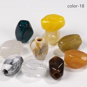 Pode incluir: Uma coleção de contas coloridas de formato irregular em várias cores, incluindo amarelo, verde, castanho e branco. As contas têm um acabamento brilhante e são exibidas sobre um fundo branco. O texto "color-18" está no canto superior direito.