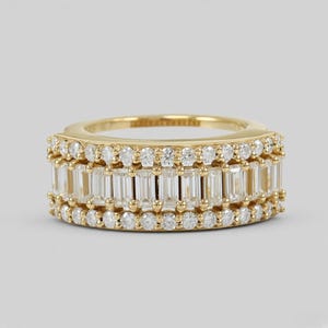 May include: A gold band ring featuring a central row of baguette-cut clear stones flanked by two rows of round brilliant-cut clear stones. The metal has a polished yellow gold finish, and the stones are set in a multi-row channel and prong design.