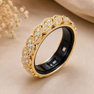 May include: A gold-toned ring featuring a series of leaf-shaped settings, each embedded with small clear stones. The outer band has a decorative beaded edge, while the inner surface of the ring is smooth, black, and contains small electronic sensors.
