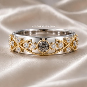 May include: A silver-toned band ring featuring a central dark grey round-cut stone surrounded by smaller clear round-cut stones set in a yellow gold-toned crisscross lattice design. The text NEOCARATJEWELRY is printed above the ring.
