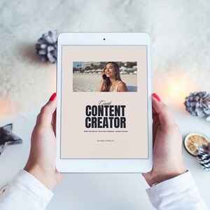 Peut inclure: Une tablette blanche affichant un guide intitulé « Content Creator » avec une photo d'une femme à l'écran. La tablette est tenue par des mains avec du vernis à ongles rouge. Des pommes de pin décoratives et un ornement en forme d'étoile sont en arrière-plan.