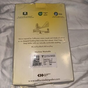 Puede incluir: Caja de cartón para un par de almohadas, con texto y gráficos. La caja presenta un dibujo de un puente y un velero. El texto incluye "Machine Washable" y "#LiveYourBestLifeEveryDay". El color de la almohada es Taupe.