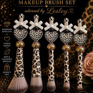 May include: A set of five makeup brushes with leopard print handles and heart-shaped accents. The brushes have white bows and are adorned with Lesley's signature. The text reads "Leopard Heart Makeup Brush Set" and "Beauty with an Edge."