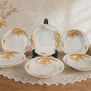 May include: A collection of six white porcelain bowls featuring a floral pattern in orange, yellow, and green. Each bowl has a gold rim and is displayed on a white lace doily. The bowls, of different sizes, are ideal for serving soups or salads.