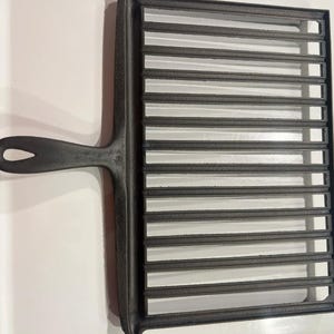 May include: A black cast iron grill pan with a long handle and a rectangular grilling surface. The grilling surface has multiple parallel raised ridges. The handle has a hole for hanging.