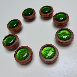 Puede incluir: Ocho tiradores de armario de madera con una base redonda de madera oscura y un centro de vidrio verde vibrante y texturizado. Los tiradores están dispuestos en un patrón circular sobre un fondo blanco.