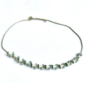 May include: A silver-toned necklace with a series of cone-shaped elements, each adorned with small, light blue gemstones. The necklace has a delicate chain and a simple clasp, suitable for formal or casual wear.