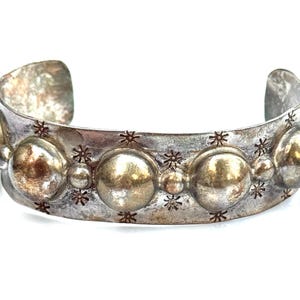 May include: A silver cuff bracelet with a distressed finish. The bracelet features large, round, raised embellishments and smaller star-shaped details. The open design allows for easy wear. A statement piece of jewelry.