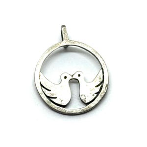May include: A silver pendant featuring two doves kissing within a circular frame. The doves are stylized with open wings, and the pendant has a loop at the top for a chain. The design is simple and elegant.