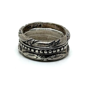 May include: A stack of three silver rings with intricate designs. The top ring features a twisted rope pattern, the middle ring has small bead-like details, and the bottom ring has an oval leaf pattern. The rings are set against a white background.