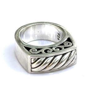 May include: A silver ring with a rectangular face. The ring features a twisted rope design on the bottom and a black inlay with a scroll design. The inside of the ring is stamped with "925".