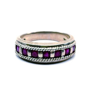 May include: A silver band ring featuring a central row of small, round, deep pink gemstones set between two twisted rope-style metal borders. The metal has a polished finish, and the design creates a textured, layered appearance around the finger.