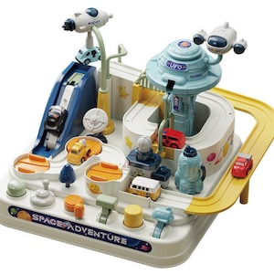 May include: A colorful plastic toy playset with a space adventure theme. The set includes a track, ramps, and various miniature vehicles, including cars and a rocket. The base of the toy has the words "SPACE ADVENTURE".