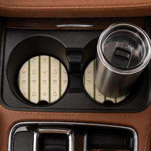 Puede incluir: Dos posavasos circulares para portavasos de coche con un patrón de rayas verticales en color crema y verde oliva, decorados con pequeños iconos ecuestres dorados que incluyen lazos, herraduras y cascos de montar. Un vaso de acero inoxidable.