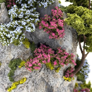 May include: A close-up of a miniature rock formation with a variety of green, pink, and white foliage. The rock is textured and gray.