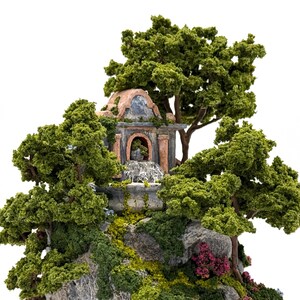 May include: A miniature stone building with a fountain and a domed roof, surrounded by lush green trees and foliage. The building is decorated with red and brown accents, and the fountain is flowing with water.
