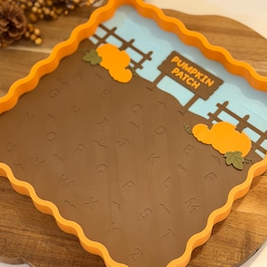 May include: A square orange tray with wavy edges featuring a brown base embossed with the alphabet letters A through Z. The tray includes a light blue sky background, a brown fence, two orange pumpkins, and a sign that reads PUMPKIN PATCH.