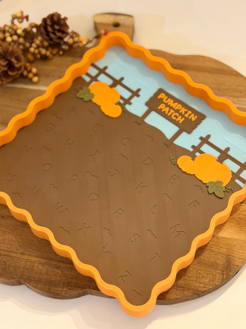 May include: A square orange tray with wavy edges featuring a brown base embossed with the alphabet letters A through Z. The tray includes a light blue sky background, a brown fence, two orange pumpkins, and a sign that reads PUMPKIN PATCH.