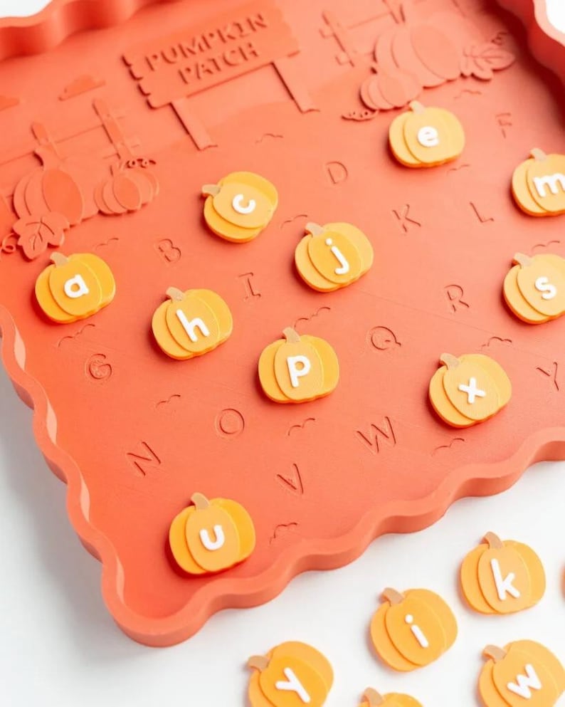 May include: A rectangular orange tray with a scalloped edge featuring a raised PUMPKIN PATCH sign and embossed letters. Several orange pumpkin-shaped pieces with white lowercase letters are placed on the tray, with additional pieces nearby.