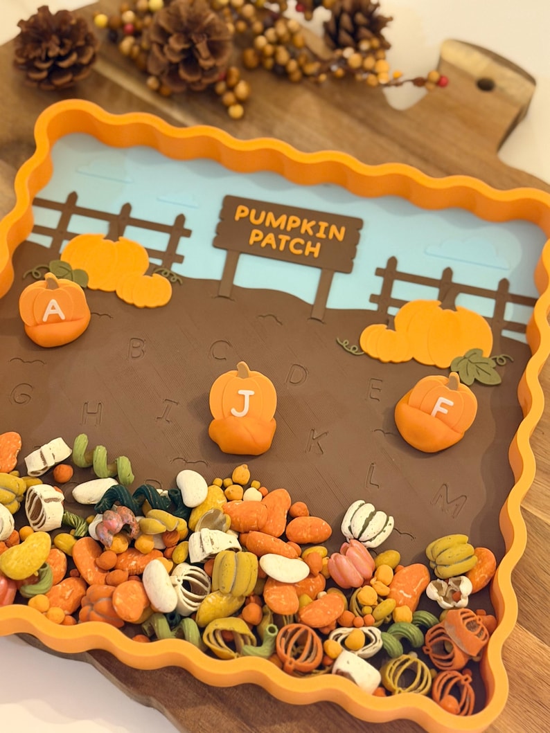 May include: A square orange tray with a scalloped edge featuring a pumpkin patch scene. The tray contains a brown field with letters A through M, a sign reading PUMPKIN PATCH, and three orange pumpkin figures labeled A, J, and F.