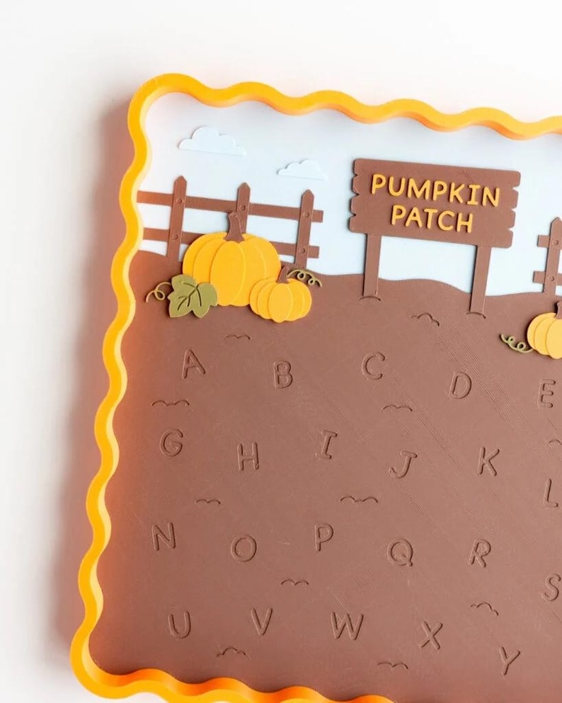 May include: A square tray with a wavy yellow border featuring a brown field with embossed letters of the alphabet from A to Y. The scene includes a brown wooden fence, a sign that reads PUMPKIN PATCH, and several orange pumpkins.