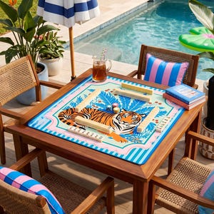 Puede incluir: Una mesa de juego cuadrada de madera con un tablero de juego colorido con tem&aacute;tica de tigre. La mesa est&aacute; rodeada de cuatro sillas de mimbre y una sombrilla a rayas azules y blancas. Una piscina est&aacute; en el fondo.