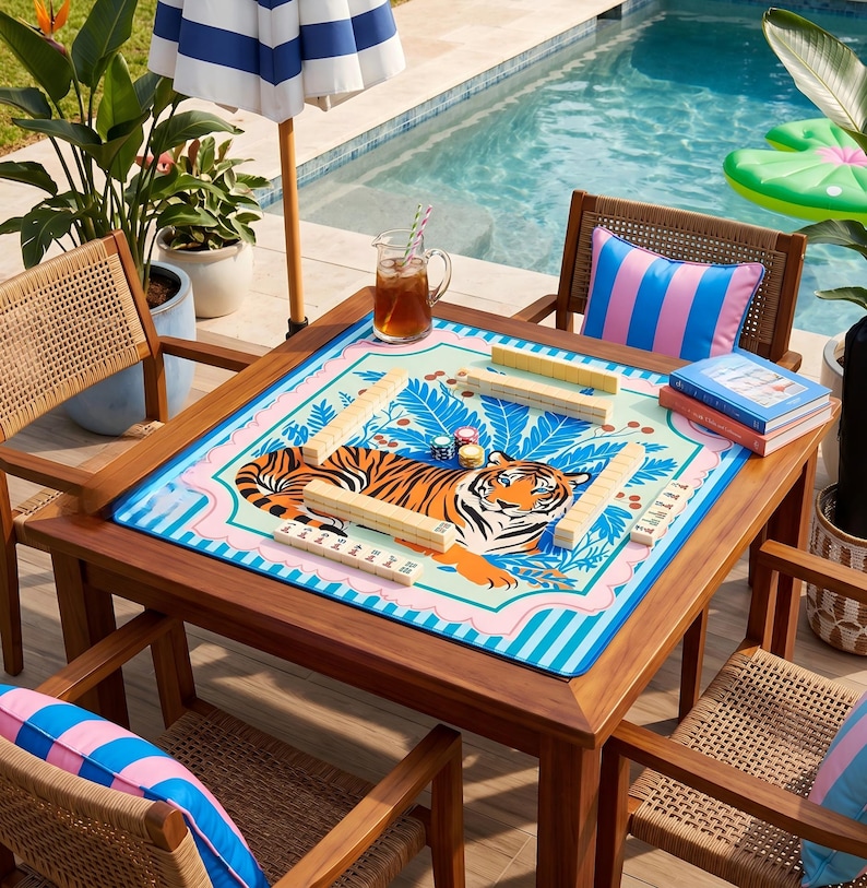 Puede incluir: Una mesa de juego cuadrada de madera con un tablero de juego colorido con tem&aacute;tica de tigre. La mesa est&aacute; rodeada de cuatro sillas de mimbre y una sombrilla a rayas azules y blancas. Una piscina est&aacute; en el fondo.