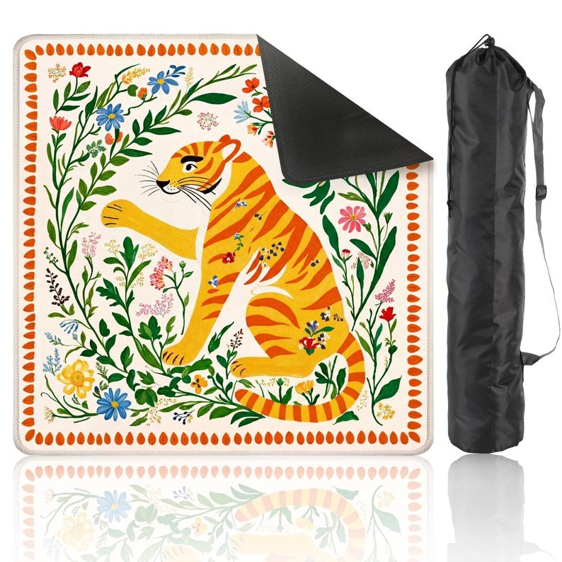 May include: A decorative yoga mat featuring a vibrant tiger illustration in orange and yellow, surrounded by colorful flowers and green foliage. The mat has a cream-colored background with a black underside and comes with a black carrying bag.