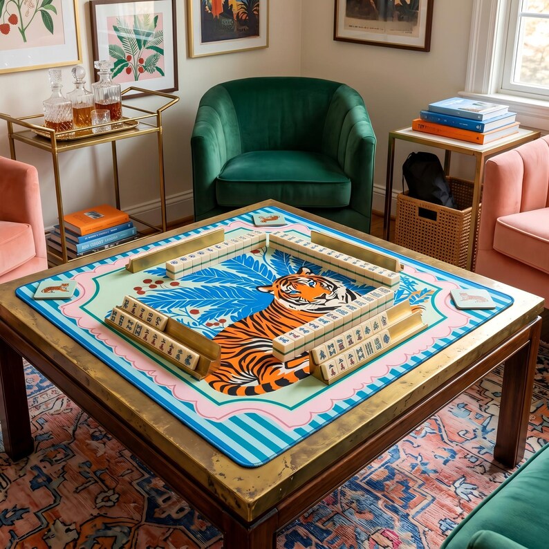 Puede incluir: Una mesa de centro cuadrada de madera con un marco de metal color lat&oacute;n. La mesa presenta un tablero de juego de mahjong colorido con un dise&ntilde;o de tigre. Las piezas del juego est&aacute;n dispuestas en el tablero. La habitaci&oacute;n tiene un sill&oacute;n verde de terciopelo y sillas rosas.