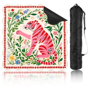 May include: A pink and red tiger illustration on a cream-colored yoga mat, surrounded by floral elements. The mat has a scalloped edge with red dots. A black carrying bag is included.