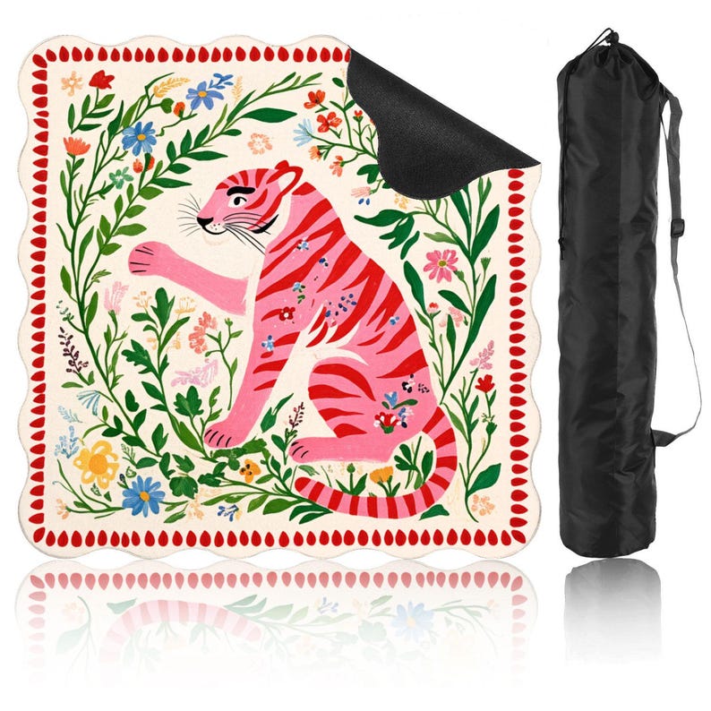 May include: A pink and red tiger illustration on a cream-colored yoga mat, surrounded by floral elements. The mat has a scalloped edge with red dots. A black carrying bag is included.