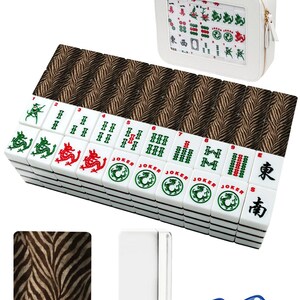 Może przedstawiać: Biały zestaw do gry w Mahjong z uchwytem na kafelki z nadrukiem w zebrę i pasującą walizką. Zestaw zawiera białe kafelki z zielonymi, czerwonymi i czarnymi symbolami, dwie niebieskie kostki i biały uchwyt na kafelki.
