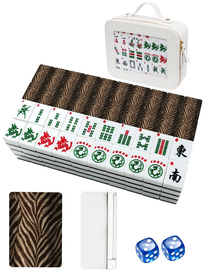 Może przedstawiać: Biały zestaw do gry w Mahjong z uchwytem na kafelki z nadrukiem w zebrę i pasującą walizką. Zestaw zawiera białe kafelki z zielonymi, czerwonymi i czarnymi symbolami, dwie niebieskie kostki i biały uchwyt na kafelki.