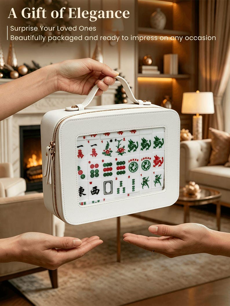 Puede incluir: Un juego de Mahjong blanco en un estuche cuadrado con asa y cremallera dorada. El juego incluye fichas con s&iacute;mbolos rojos, verdes y negros. El texto en el estuche dice "A Gift of Elegance".