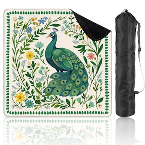 May include: A square picnic blanket featuring a peacock design with a green and blue color palette. The peacock is surrounded by floral elements in yellow, blue, and pink. Includes a black carrying bag.