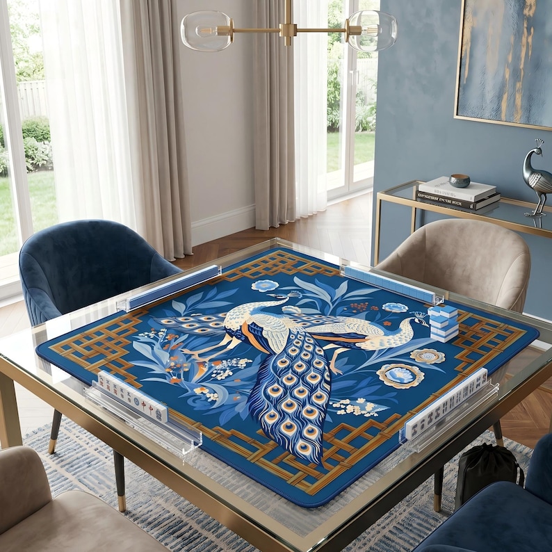 May include: A square, glass-topped table with a blue peacock-themed game board. The board features a detailed peacock design in shades of blue, white, and gold. The table is set in a well-lit room with chairs and decorative elements.