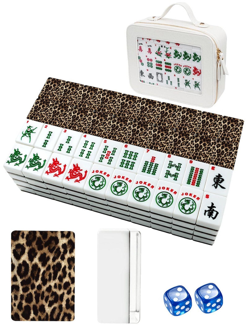 Puede incluir: Un juego de Mahjong blanco con una alfombra con estampado de leopardo y un estuche a juego. El juego incluye fichas blancas con s&iacute;mbolos verdes, rojos y negros, dos dados azules y un soporte blanco para fichas.