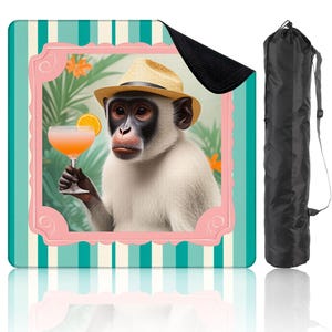 Puede incluir: Una manta de playa con un mono con sombrero de paja y un cóctel. La imagen está enmarcada en rosa y sobre un fondo a rayas turquesa y blanco. Incluye una bolsa de transporte negra.