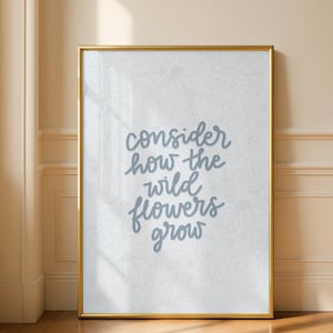Puede incluir: Un estampado enmarcado con un marco dorado. El estampado presenta el texto "consider how the wild flowers grow" en un estilo manuscrito, en color azul claro. El fondo tiene un patrón floral.